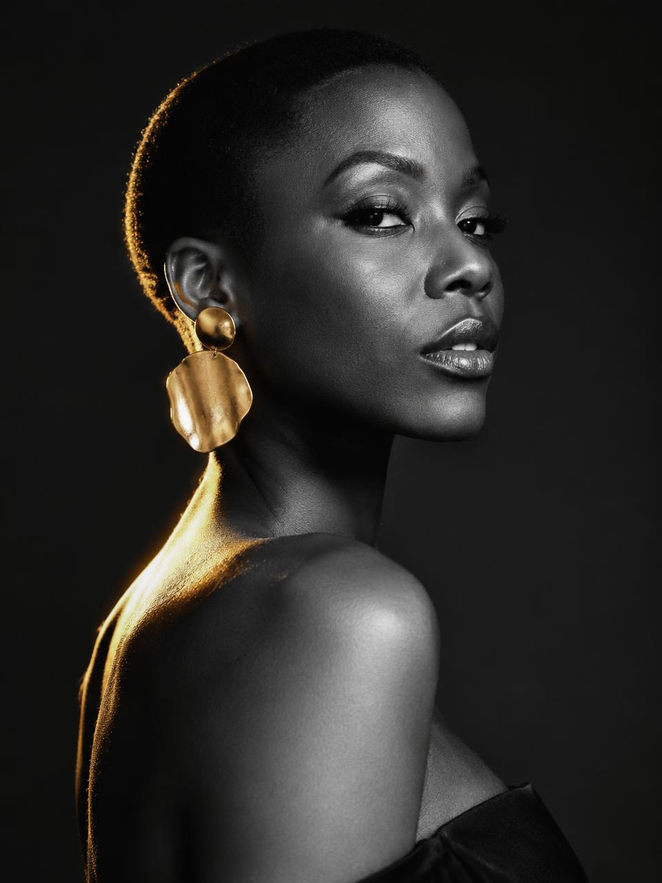 Black and white editorial portrait with sculptural gold earrings and warm rim light